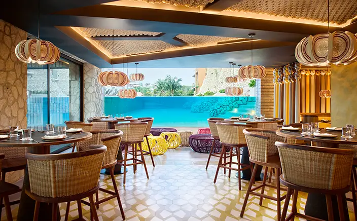 Open-air restaurant with woven pendant lighting and poolside view at Hotel Xcaret Arte, highlighting modern Mexican design, immersive dining spaces, and adults-only all-inclusive luxury in Riviera Maya.