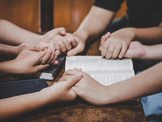 Hands held in prayer over a bible study session.