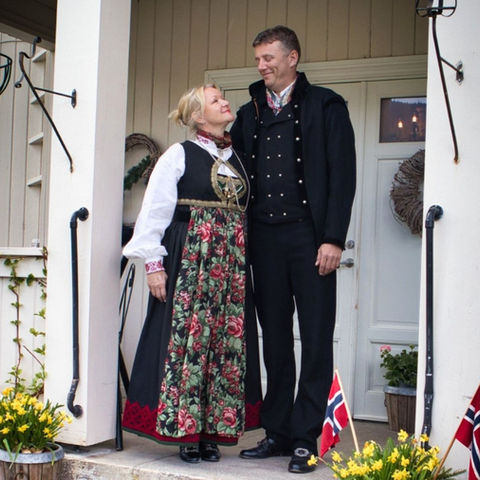 Norsk par i bunad på veranda med flagg.