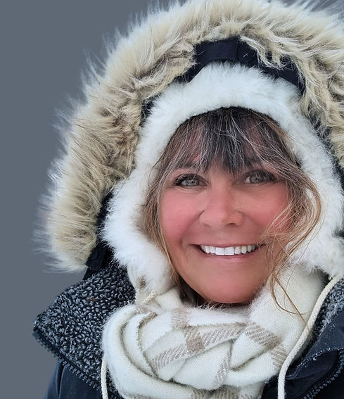 A smiling AK Magraff hikes in light snow, wearing a blue winter jacket with a fur hood.