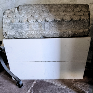 Small medieval stone headstone with inscriptions and shaped like a house.