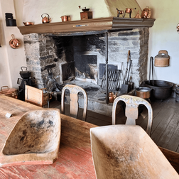 The old kitchen at Ringerike Museum featuring a large, blackened hearth, cobber pots hanging from the ceiling, and old wooden furniture.