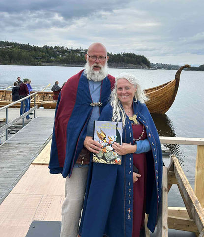 Ragnar Wergeland og Hilde Helene Wergeland kledd i vikingdrakt poserer foran Steinsfjorden i Hole kommune og vikingskipet Dronning Åsta, bygget av Hardraade vikingskipforening. .