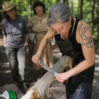 Theresa Emmerich Kamper scraping an animal hide outdoors