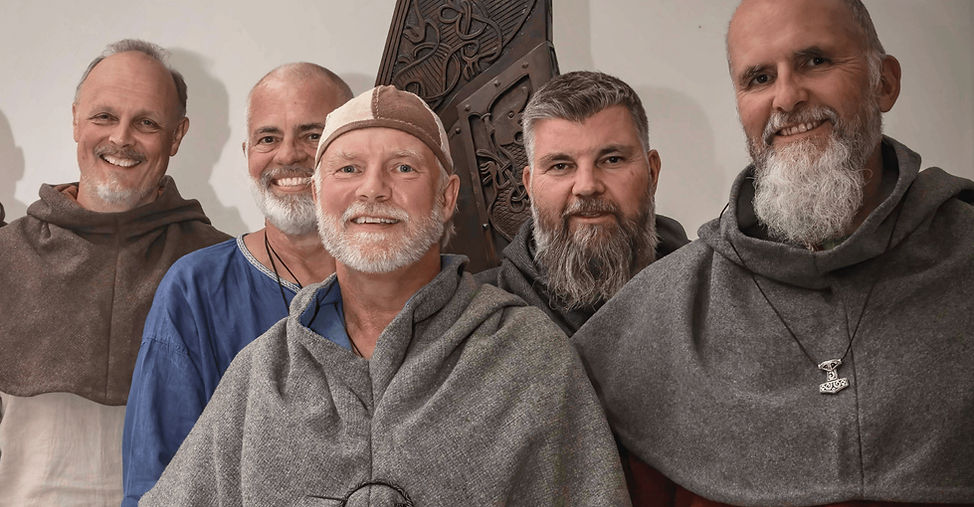 En gruppe vikinkledde menn fra Hardraade vikingskipforening står samlet foran en utskjæring i Ringriksstil. 