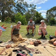 Group of people examine items;  DEER SKIN TANNING ; outdoors with items displayed.