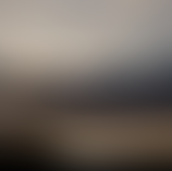 A tall wooden cross stands on a hill underneath puffy clouds with sunrays peering out.