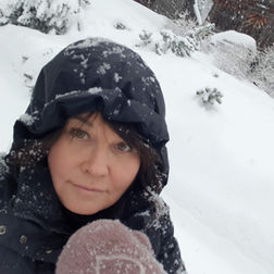 AK Magraff stands in front of her mountain house in Norway, bundled up in a big blue coat and pink wool mittens, enjoying the winter scenery.