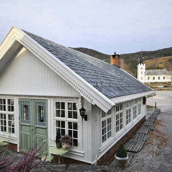 Hvit trebygning med grønne dører, kirke og fjell