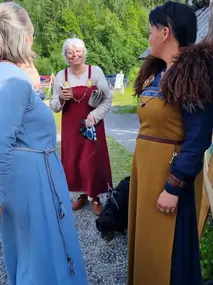 Tre damer i forskjellige fargerike vikingkjoler ler og prater sammen. 