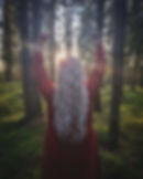 A woman with long white hair standing in a forest dressed in a red viking dress.