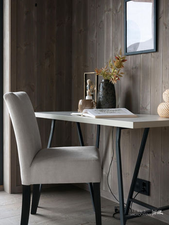 Moderne arbeidsplass med lys stol og skrivebord mot trevegg.