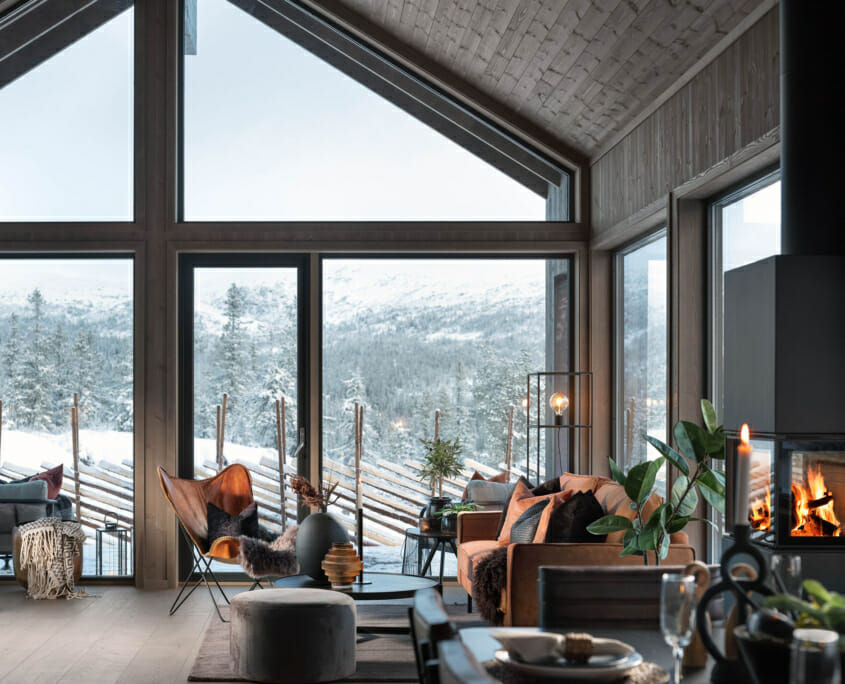 Moderne stue i en Snøhetta-hytte med store vinduer mot snølandskap.