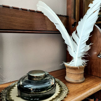 A white quill pen and ink is sitting on a table next to a black ceramic ink holder.
