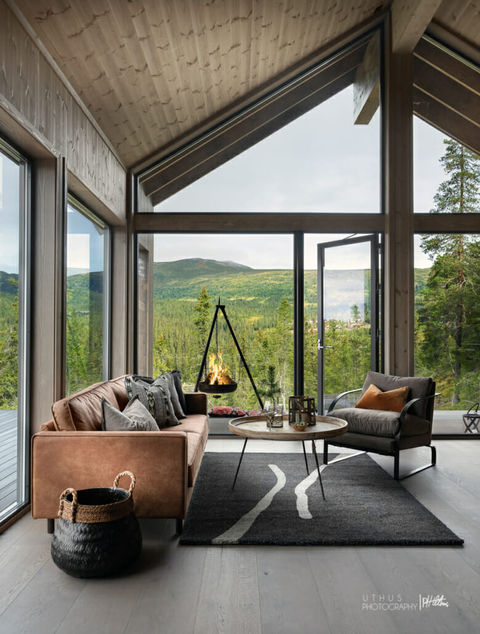Moderne stue i hytte med utsikt over skog og fjell.