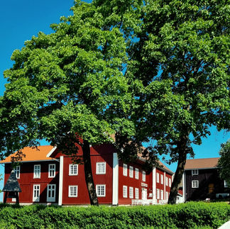 An old red painted wooden building with white windows once used as a vicarge. Now it's Ringerikes Museum. The building is situated on a hill overlooking mountains, farmlands and lakes.