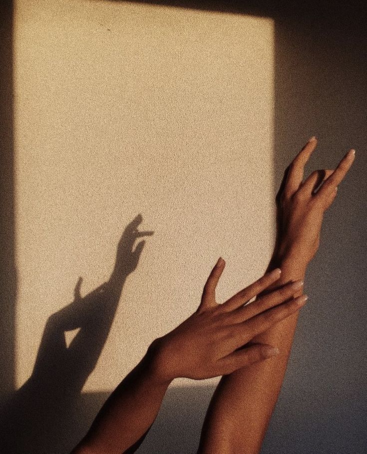 Mains levées dans une lumière dorée, projetant leur ombre sur un mur