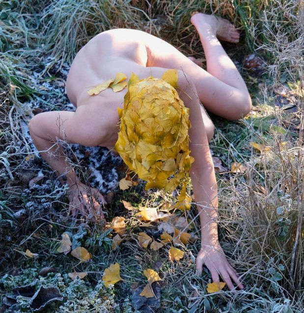 NATURE CONNECTION : EARTHBOUND - Gaby Solly, 2022 (Digital image).
A naked female figure wearing a bright yellow ‘nature-immersion-hood’, sewn out of Gingko leaves and cotton thread, crawls amongst frosty grass and leaves. 
(Photo credit: Shona Kitson)