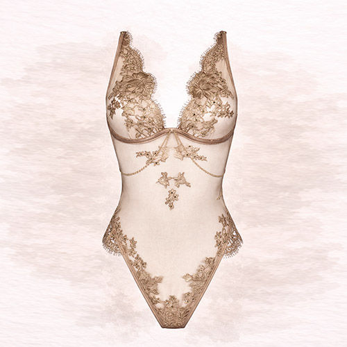 Elegant wired lace bodysuit in light gold with floral patterns, set against a soft, blurred background.