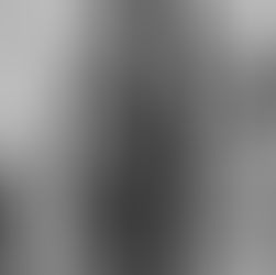 African American women with dark complexion wearing a light golden bodysuit with lace applique that appears like contrasting tattoos on her skin. She is gently taking a step and touching a window whilst looking at her own reflection.