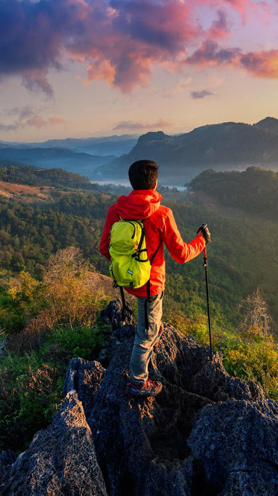 Hiker with yellow backpack overlooking a mountain valley at sunset