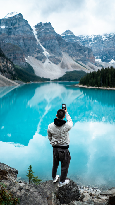 Person photographing Moraine Lake and snowy mountains