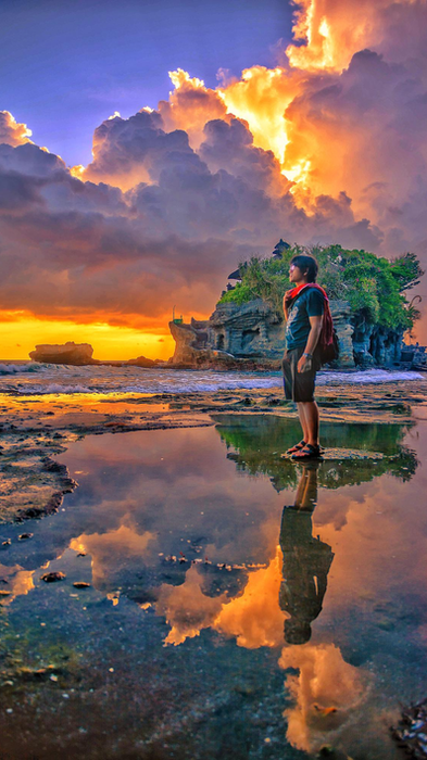 Man standing by tide pools reflecting a sunset at Tanah Lot