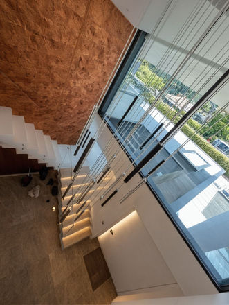 Modern staircase, white lacquered wood, glass balustrade, LED lighting, beige marble flooring, rust-effect metal wall cladding,  black and gold cylindrical pendant lights,  cord suspension,  view of  garden, neighboring houses, green trees,  cars,  summer, daylight.