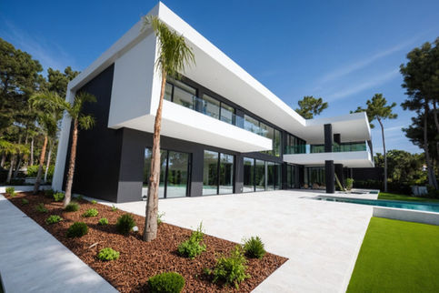 Modern house, white and black stucco, large windows, glass railings, infinity pool, landscaping with palm trees, pine trees, shrubs, wood chips, lawn,  artificial turf, sunny day.