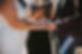 A closeup of an LGBT couple holding hands during a wedding ceremony. The officiant holds a book in the background