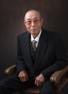 椅子に座るスーツ姿のシニア男性の肖像写真