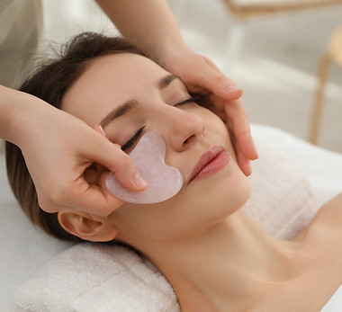Young woman receiving facial massage with gua sha tool in beauty salon.jpg