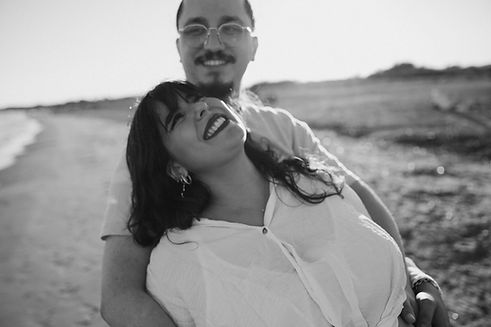 Photo en noir et blanc d'un couple qui s'enlace sur la plage, la femme enceinte dans les b