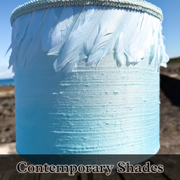 A blue silk lampshade with feather trim against a sunny scottish landscape.