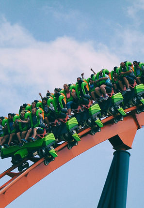 A rollercoaster with lots of people with their hands up, the rollearcoaster looks like it's coming in the direction of the reader and is red.