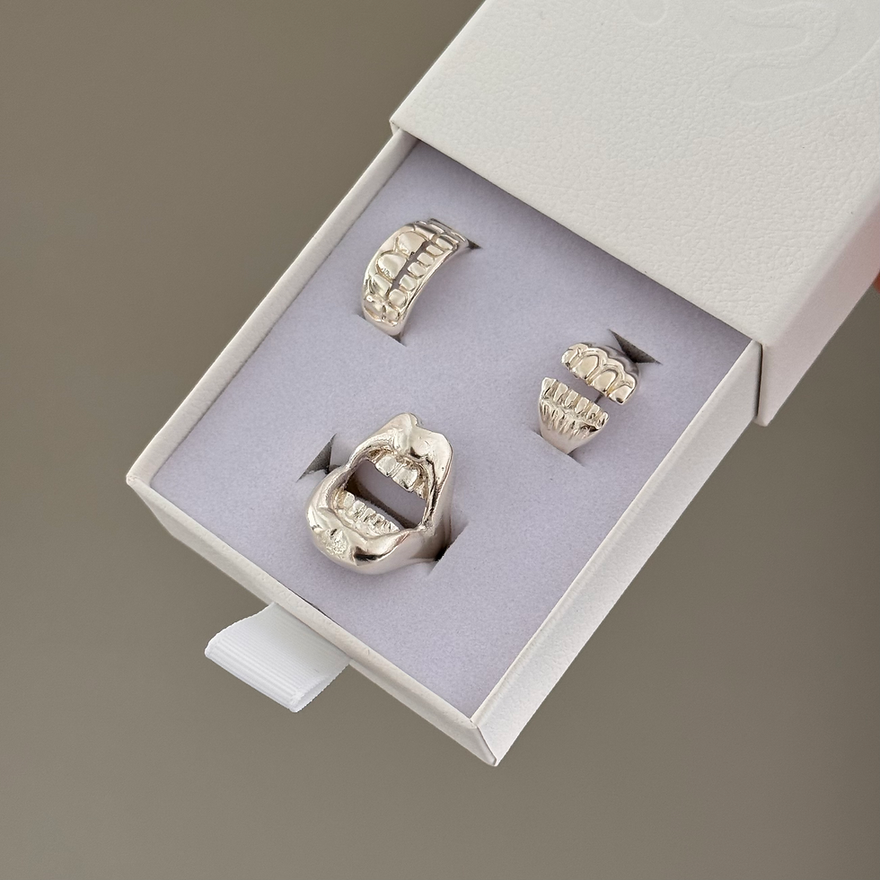 Thumbnail: A silver ring designed as an open mouth with detailed teeth is presented inside a white, textured jewelry box.