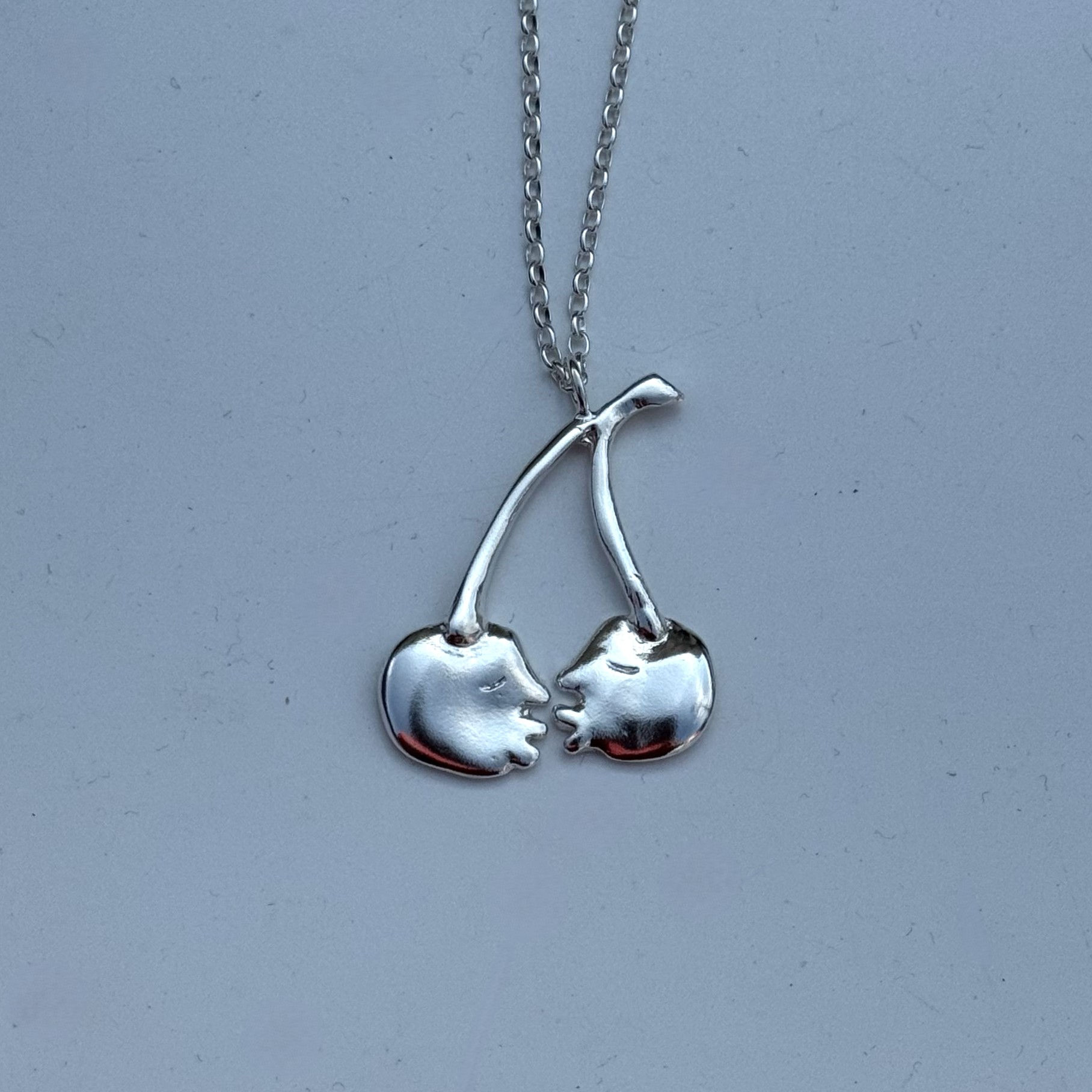 Silver cherry pendant with two sculpted faces about to kiss