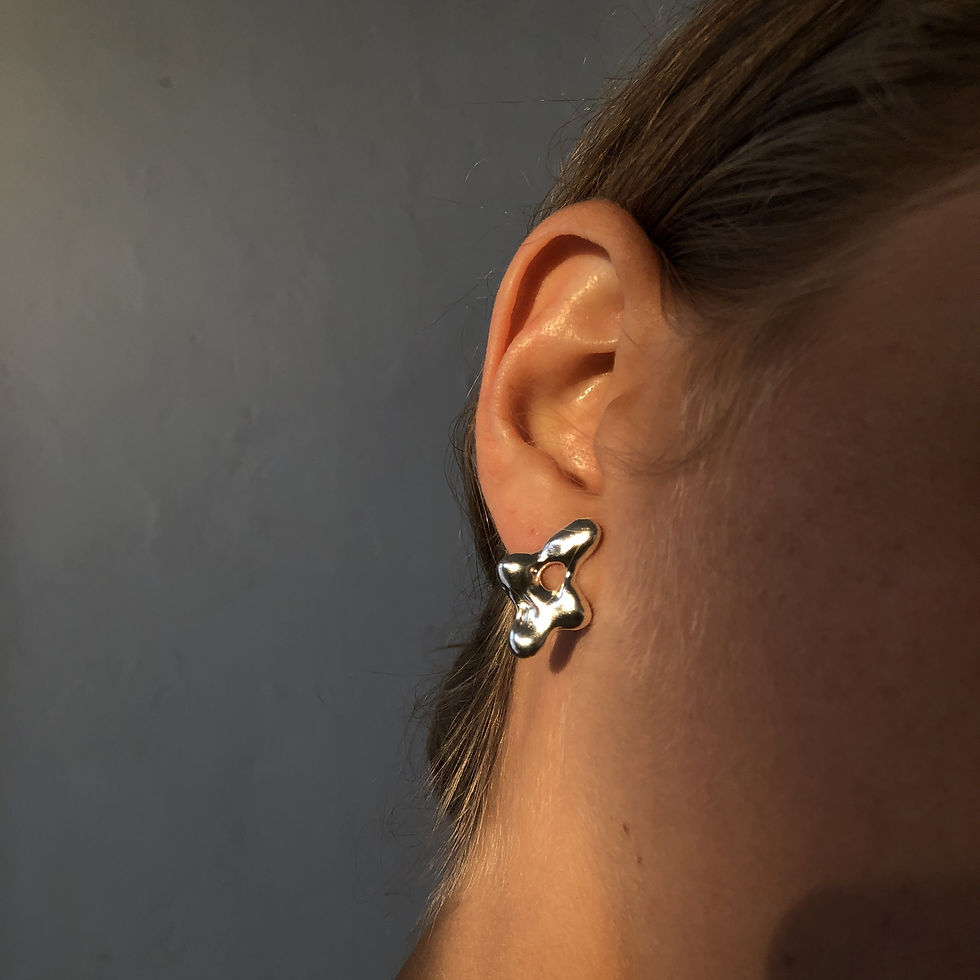 Thumbnail: Close-up of a sculptural silver earring on a woman's ear, with a soft, abstract form and central cutout.