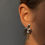 Thumbnail: Close-up of a sculptural silver earring on a woman's ear, with a soft, abstract form and central cutout.