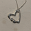 Thumbnail: Silver necklace with a sculpted open heart pendant and two round ends, tied with a small knot.