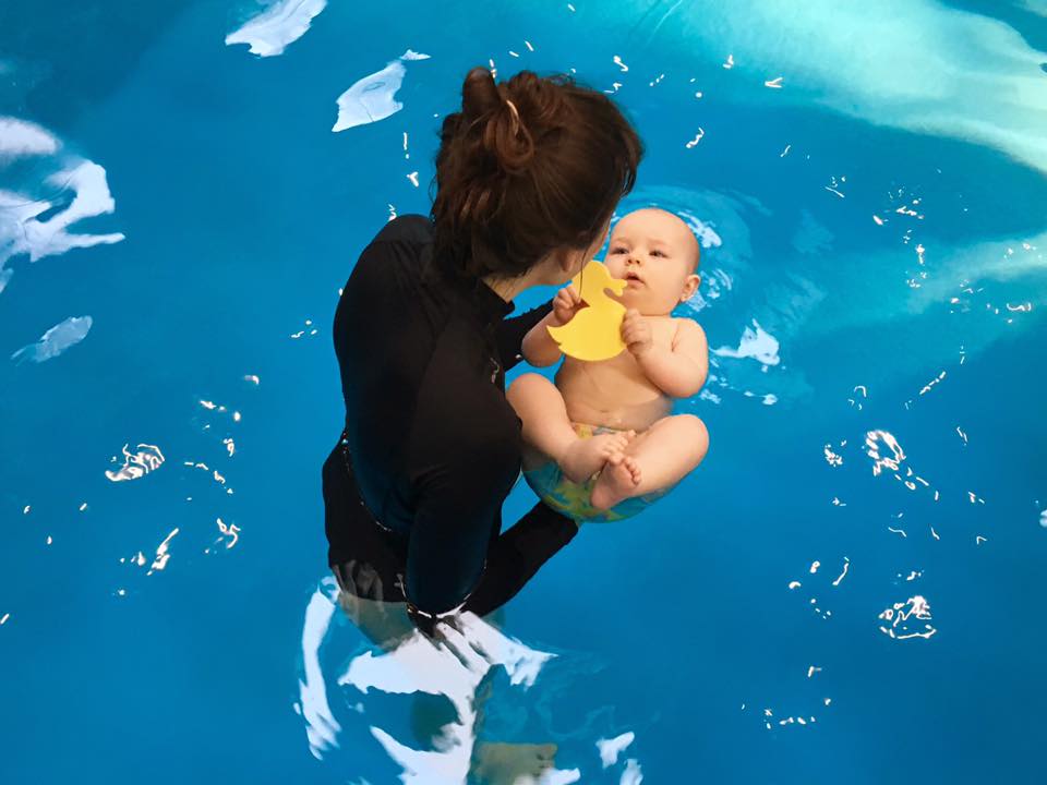 Mother holding a baby with a rubber duck in the water during a Superbaby swimming lesson