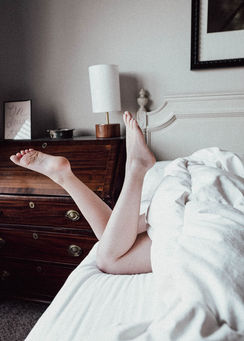 Caucasian woman's legs and bare feet kicking with the rest covered by sheets. In the background is a dresser, lamp, and headboard.
