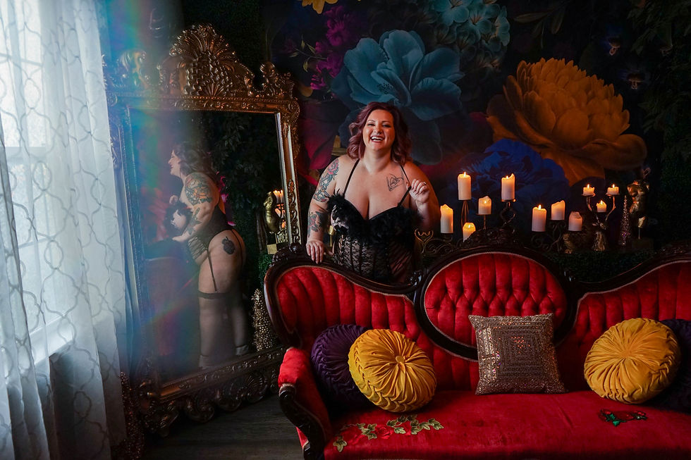 A plus size female in black lingerie standing behind a couch smiling