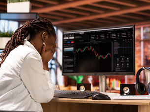 A black woman holds her head in her hands while she looks at her computer where she's losing money.