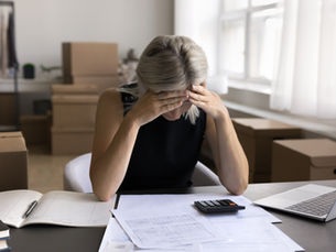 A white woman holds her head in her hands while she looks over financial statements.