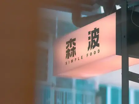 粉色發光招牌寫著“森波 SIMPLE FOOD”,懸掛在室內門店入口旁,背景虛化,氛圍安靜現代。