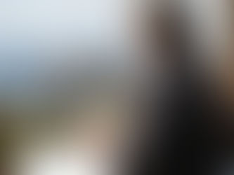 A mature woman sat on a balcony with notebook and pen, looking out to the ocean.