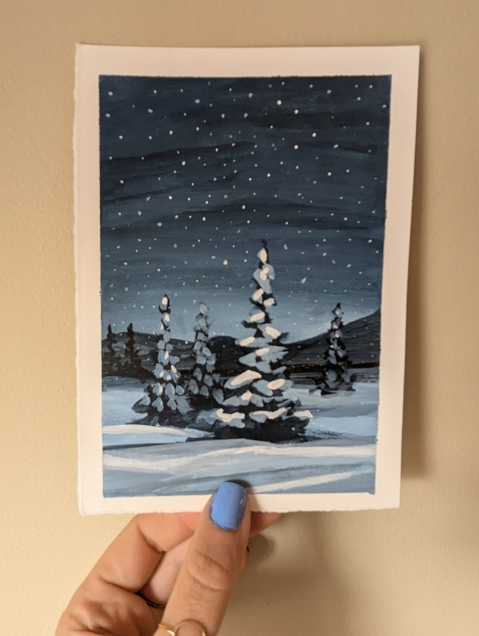 hnd holding acrylic painting of a snowy forest with a pine tree front and center. background is navy blue