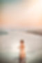 an older toddler is standing at the shoreline with a long ruffle dress on and a sunsetting sky