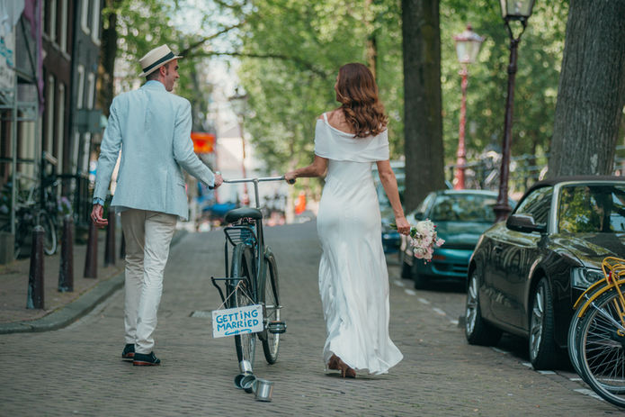 Newlywed couple walk hand in hand down a tree‑lined city street carrying a bouquet after a Cyprus wedding.